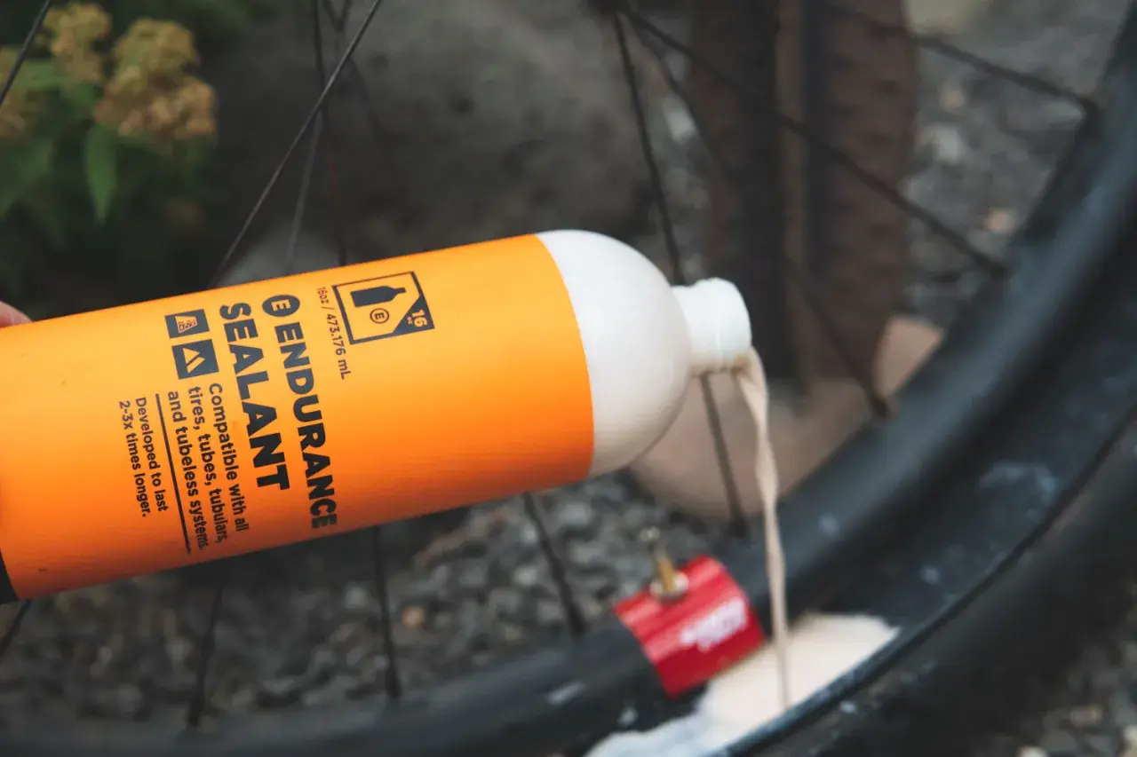 Pouring orange Endurance Sealant into a bike tire. This sealant is designed for longer-lasting protection compared to regular options.