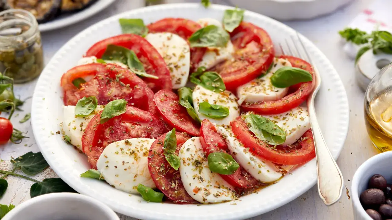 Ensalada caprese fresca con rodajas de tomate y mozzarella, aderezada con albahaca y especias.