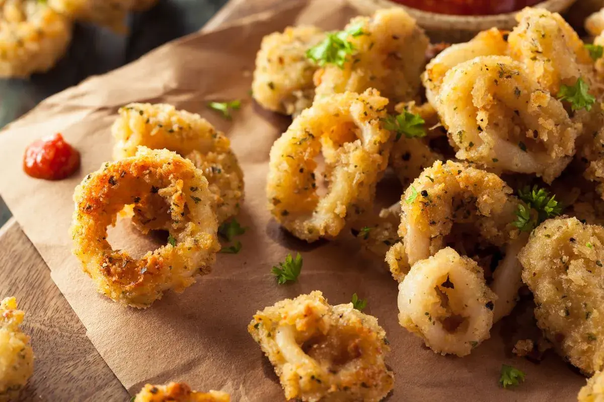 Anelli dorati e croccanti di calamari gratinati al forno, guarniti con prezzemolo fresco e accompagnati da una salsa rossa.