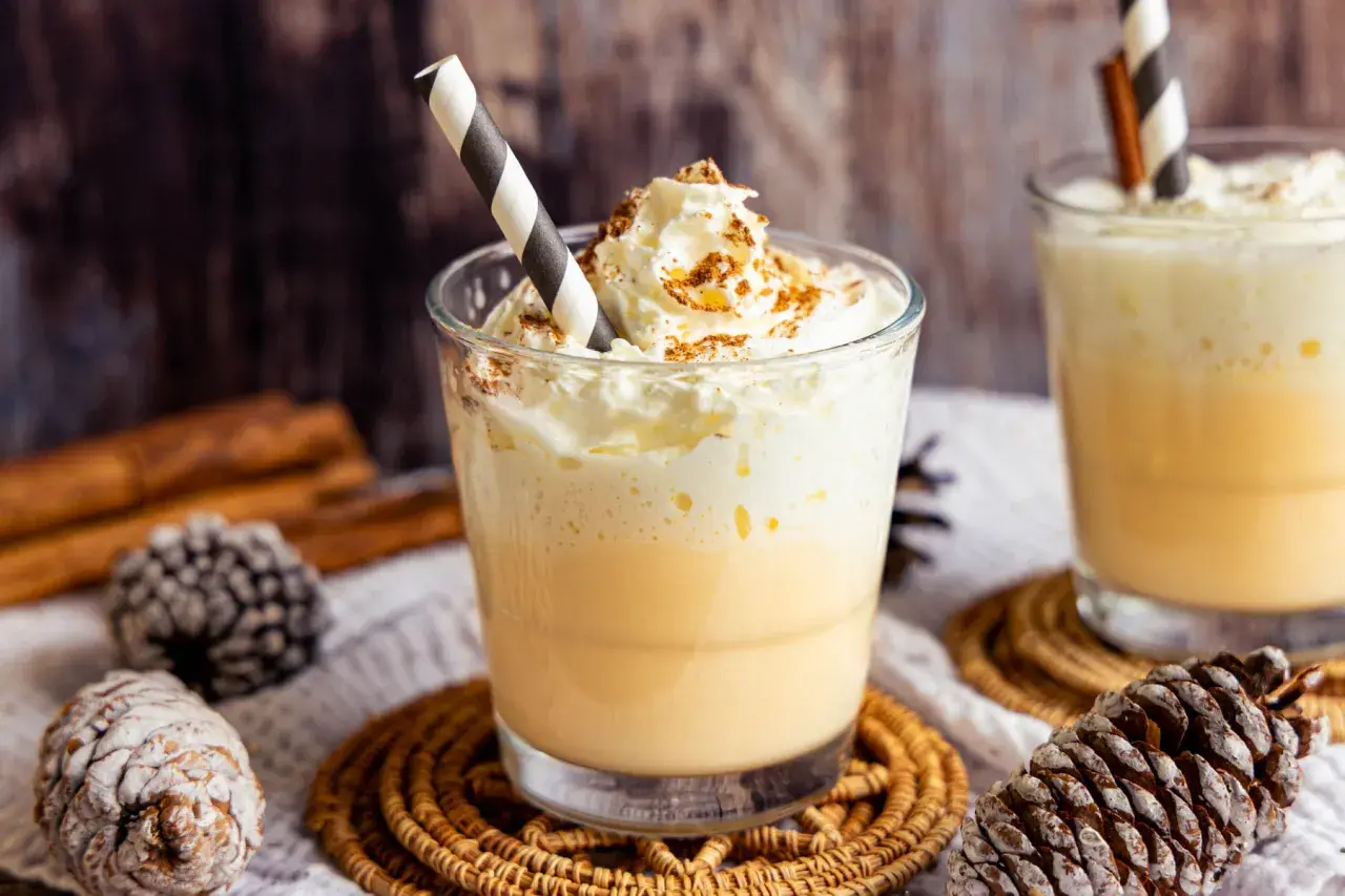 Zwei Gläser Bombardino mit Sahne und Zimt, dekoriert mit Tannenzapfen und Zimtstangen.
