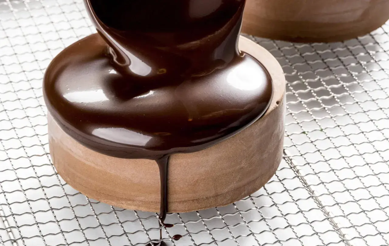 Un glaçage chocolat brillant et onctueux recouvre un petit gâteau rond, coulant sur les côtés.