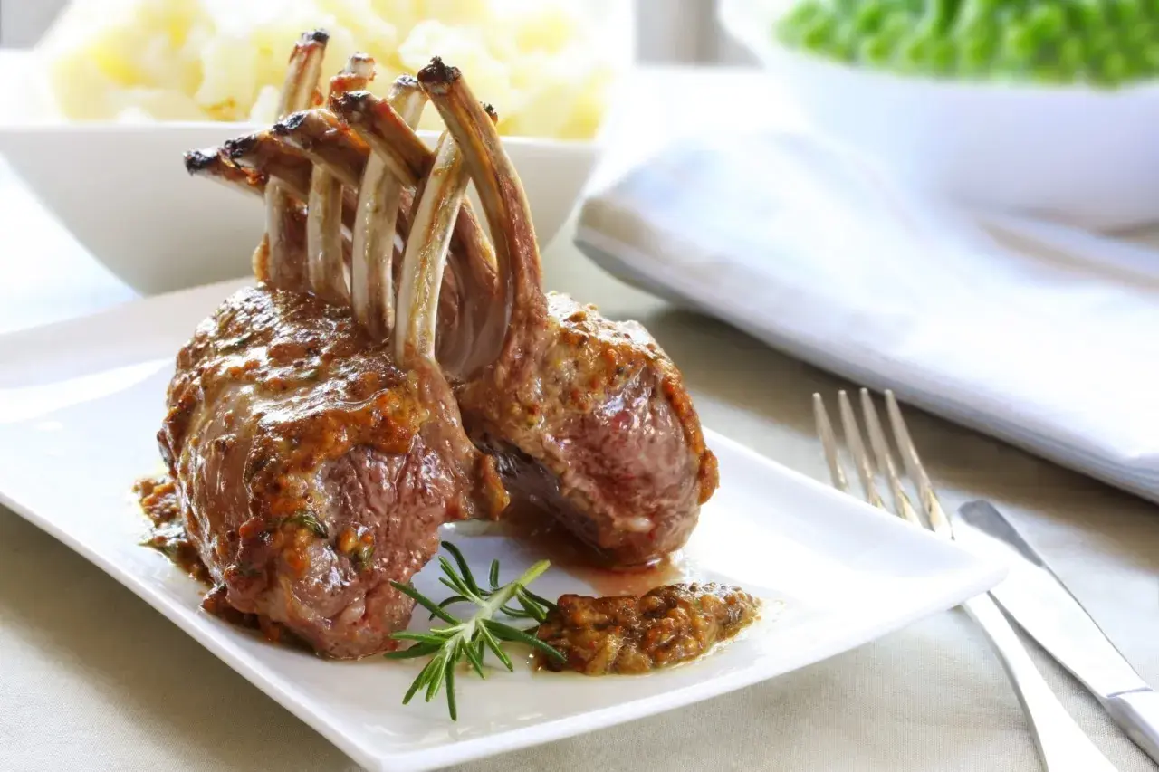 Un délicieux carré d'agneau rôti, nappé d'une sauce savoureuse, est servi avec une branche de romarin.