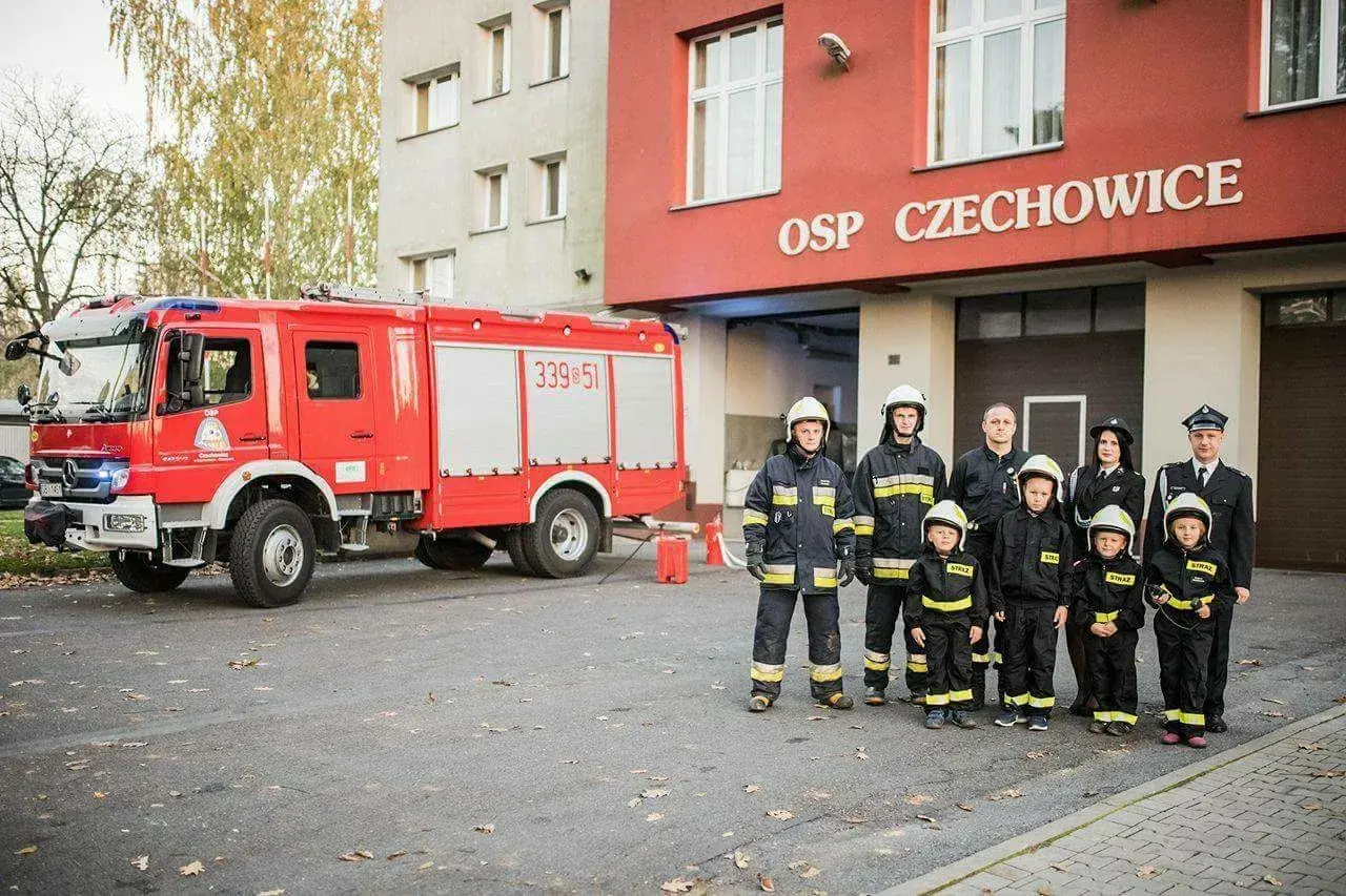 Strażacy OSP Czechowice z wozem strażackim i dziećmi w strojach strażackich.