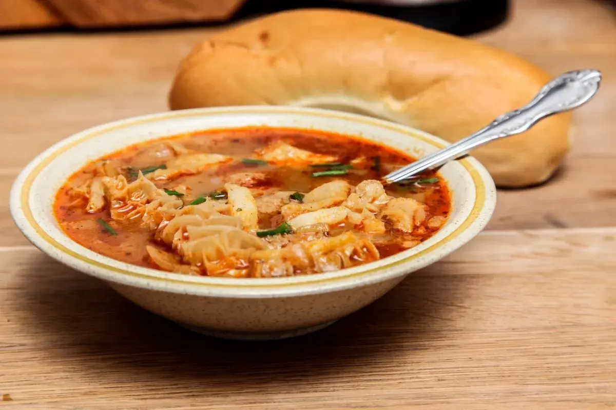Piatto fumante di trippa ricetta della nonna, con pane fresco sullo sfondo, pronto per essere gustato.