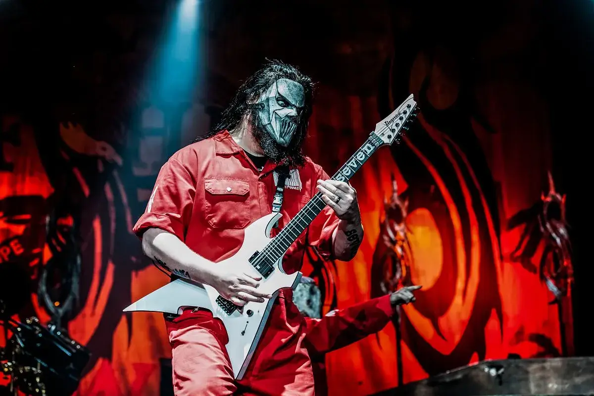 Muzyk Slipknot w czerwonym kombinezonie i masce gra na białej gitarze. Zapowiedź nowego albumu Slipknot.