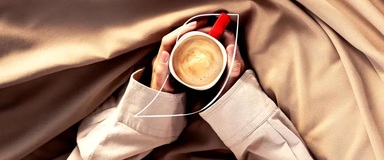 Dłonie trzymają filiżankę kawy Nescafé z bogatą cremą. Idealna kofeina na chłodny dzień.