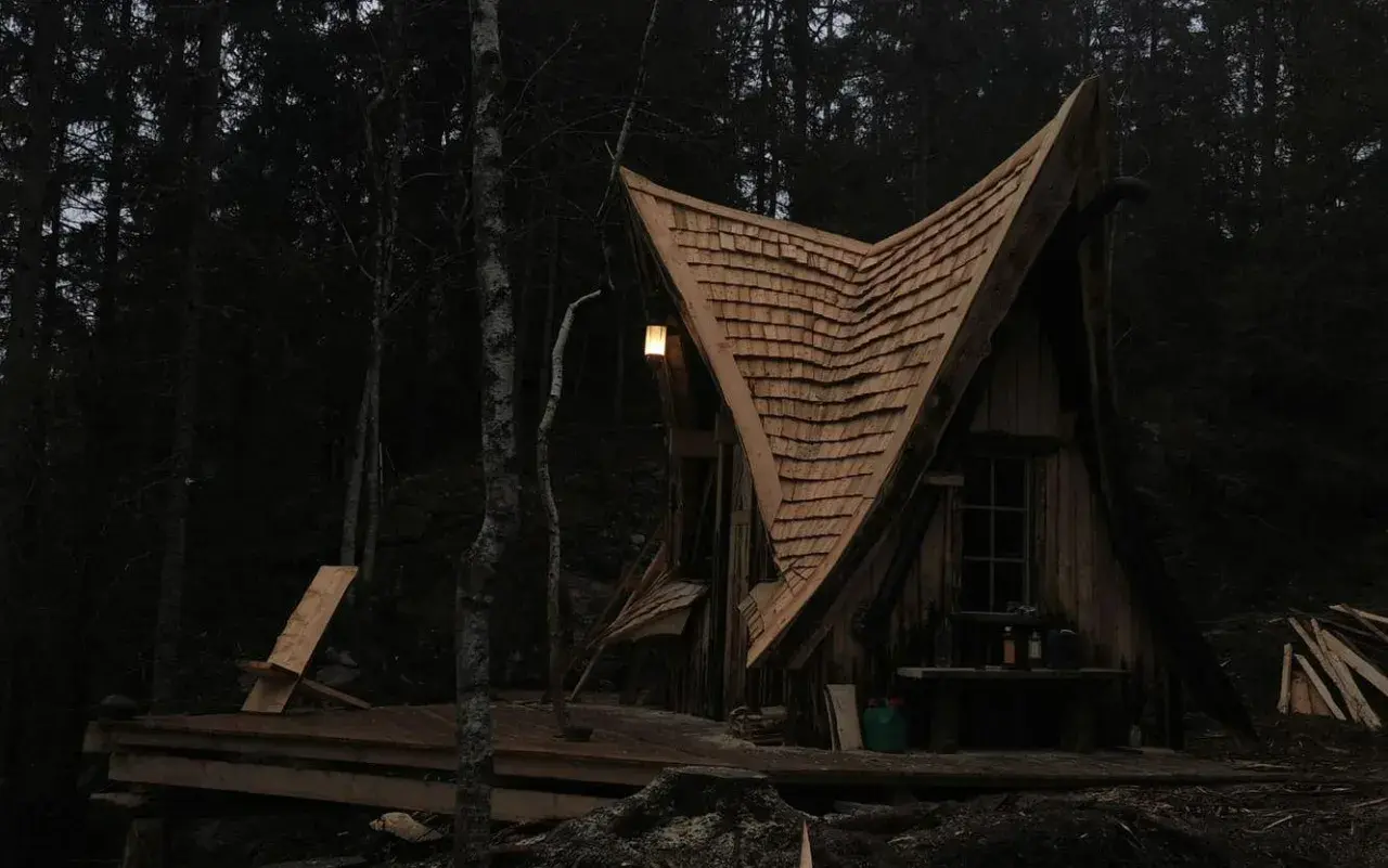 En magisk koja i skogen med ett spetsigt tak av träspån. En ensam stol står på altanen, redo för en stunds avkoppling.