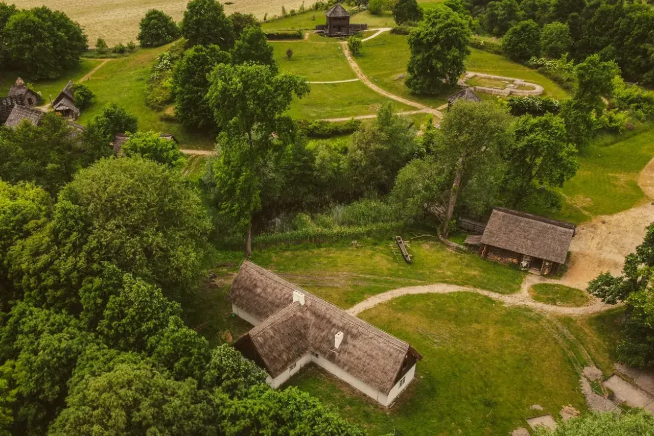 Rezerwat archeologiczny Zawodzie, z widokiem na drewniane chaty i zalesione wzgórza, ukazuje dawne osadnictwo.