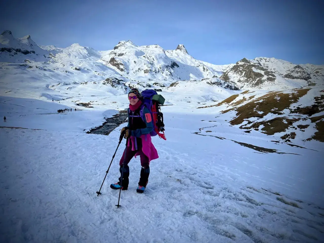 Una mujer con mochila y bastones disfruta de excursiones nieve en un paisaje montañoso cubierto de blanco.