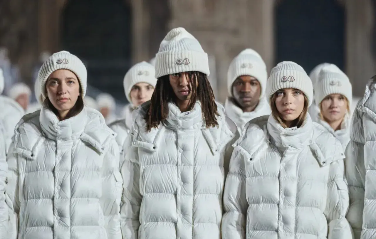 Grupa osób w białych kurtkach i czapkach Moncler. To właśnie moncler co to za firma – marka znana z luksusowej odzieży zimowej.