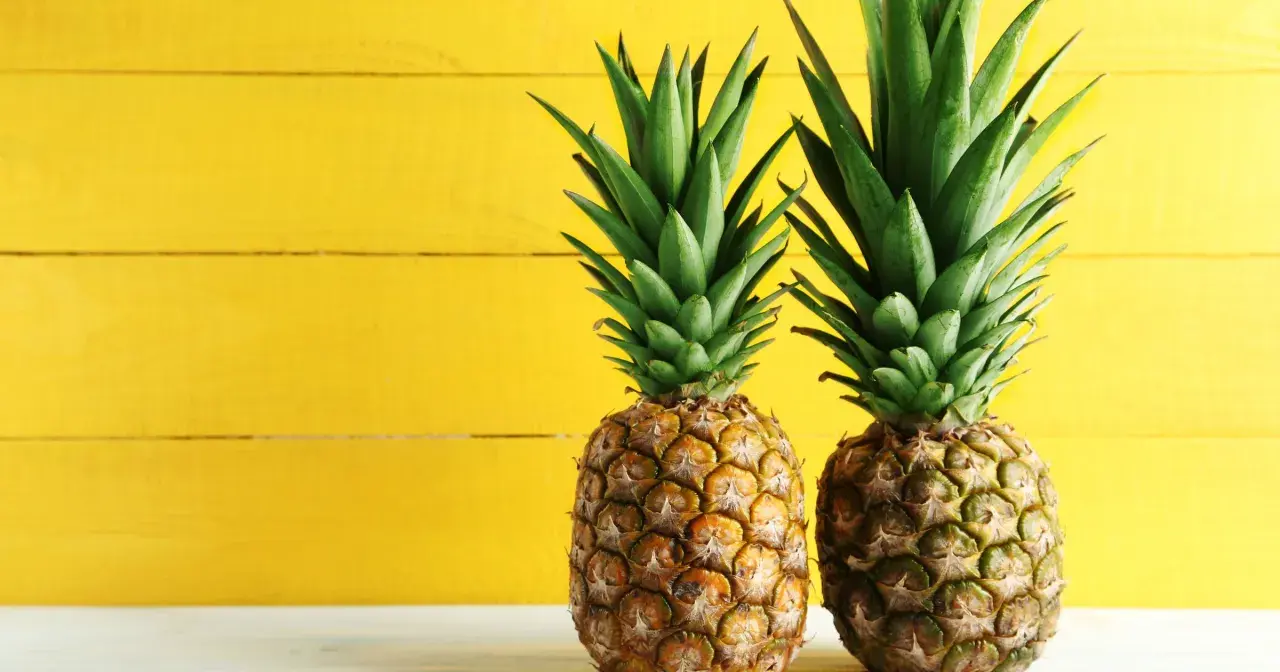 Dwa soczyste ananasy na tle żółtej deski. Poznaj ich bogactwo witamin i minerałów – ananas wartości odżywcze.