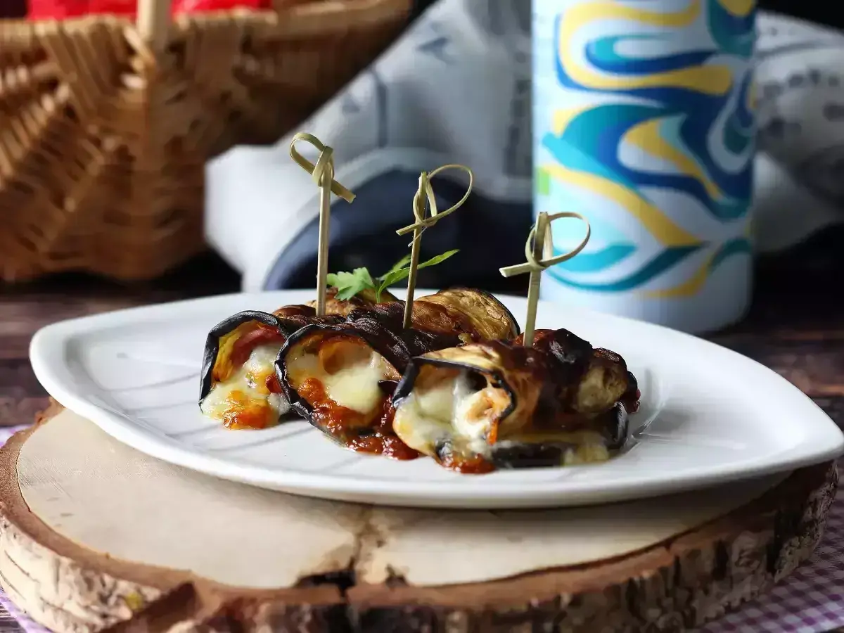 Grillad aubergine rullad med ost och tomatsås, serverad på en vit tallrik. Perfekt för picknick!