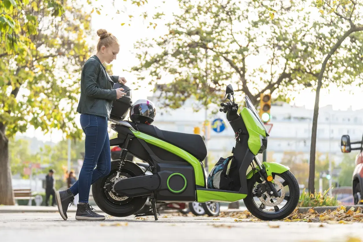 Mujer con casco y móvil junto a ciclomotor eléctrico verde. ¿Cuál será su velocidad máxima?