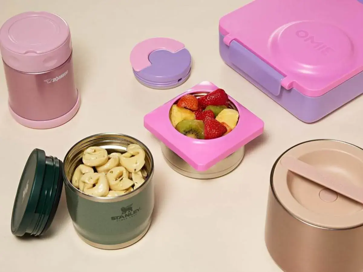 Colorful bento boxes and insulated food jars filled with pasta and fruit. These containers are designed to keep food warm for lunch.