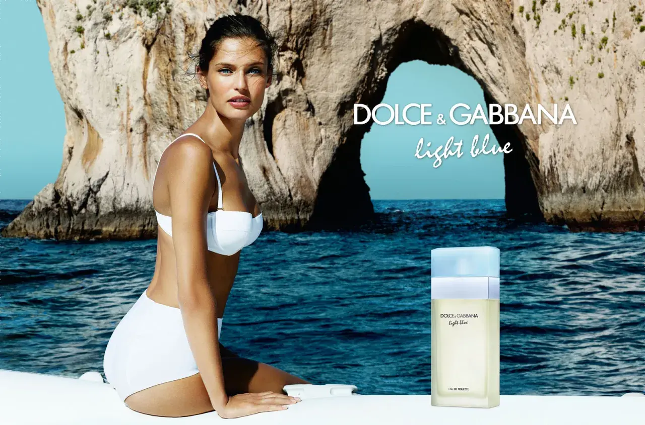 Kobieta w białym bikini na tle skalistej zatoki. Obok flakon perfum Dolce & Gabbana Light Blue.
