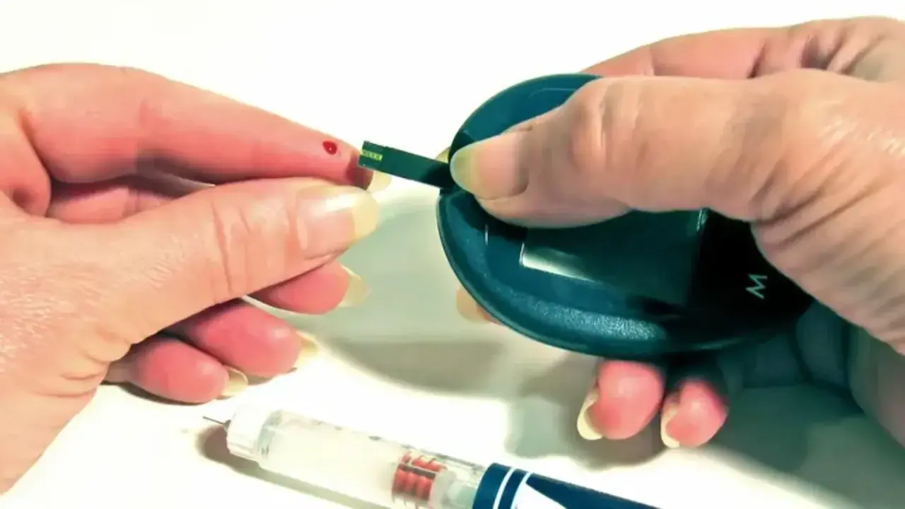Kropla krwi na palcu, pasek testowy i glukometr. Obok wstrzykiwacz z insuliną aspart sanofi.
