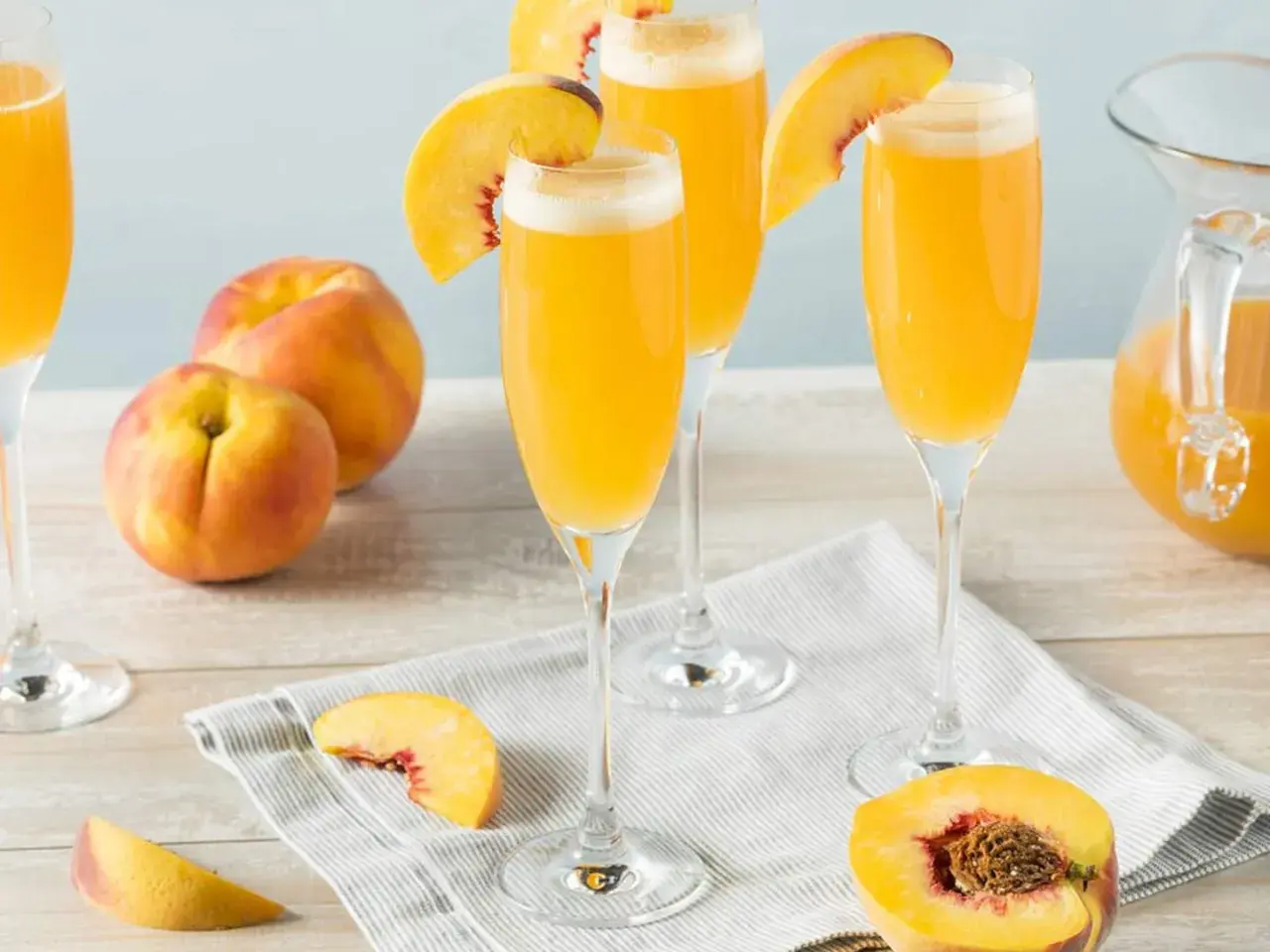 Tre glas med en gyllene drink, garnerade med persikoklyftor. Persikor och en karaff med drinken syns också.