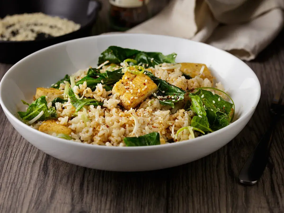 Deliciosa ensalada de arroz con trozos de tofu dorado, espinacas frescas y semillas de sésamo. Un plato nutritivo y lleno de sabor.