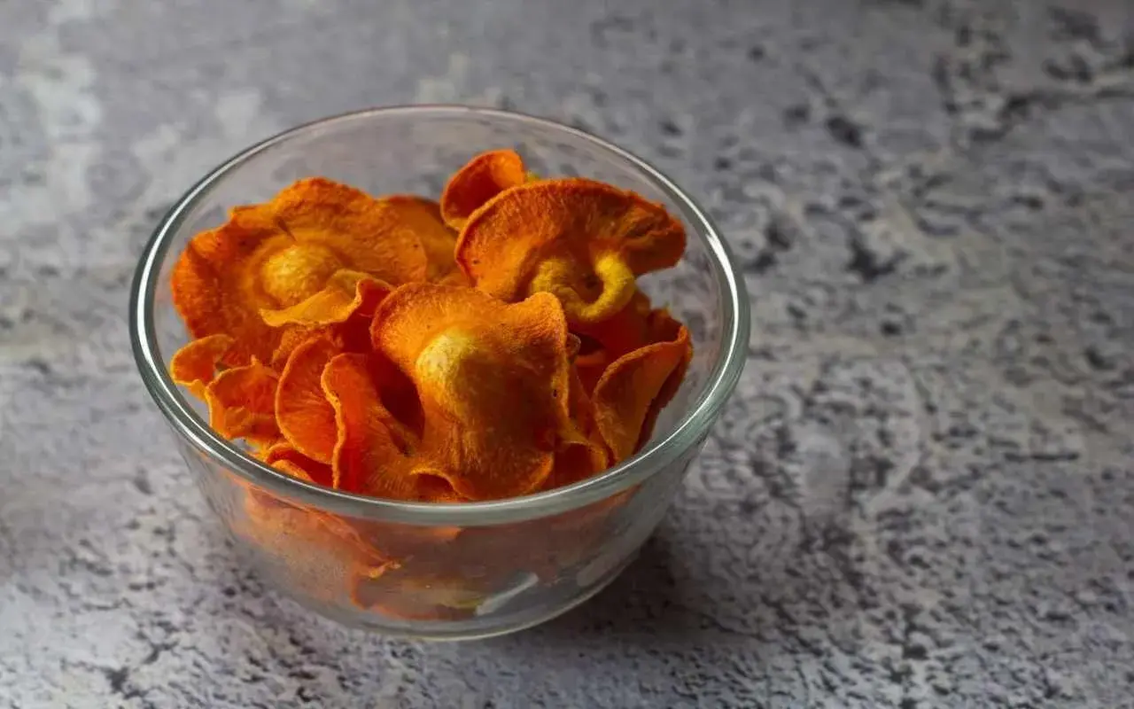 Croccanti chips di carote, preparate in friggitrice ad aria, servite in una ciotola di vetro.