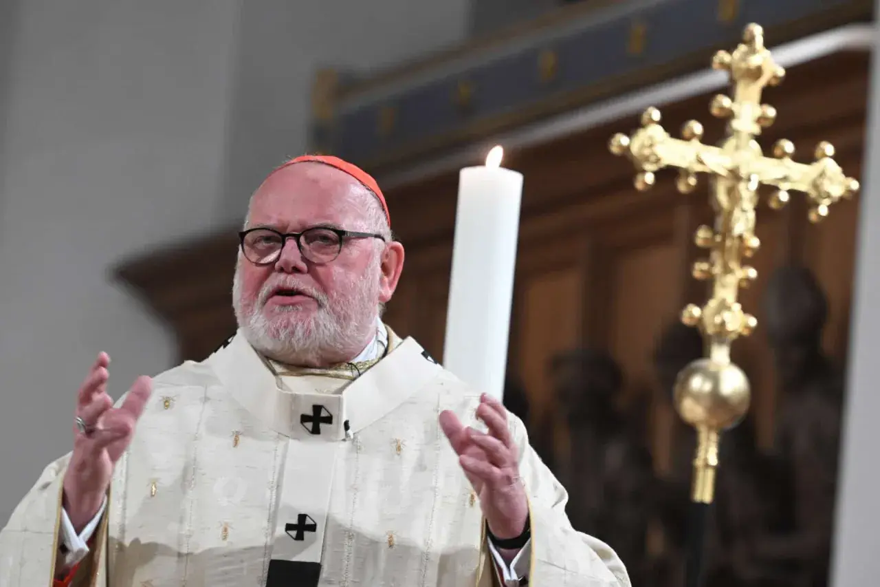 Kardinal Marx spricht in festlicher Robe vor einer Kerze und einem goldenen Kreuz.