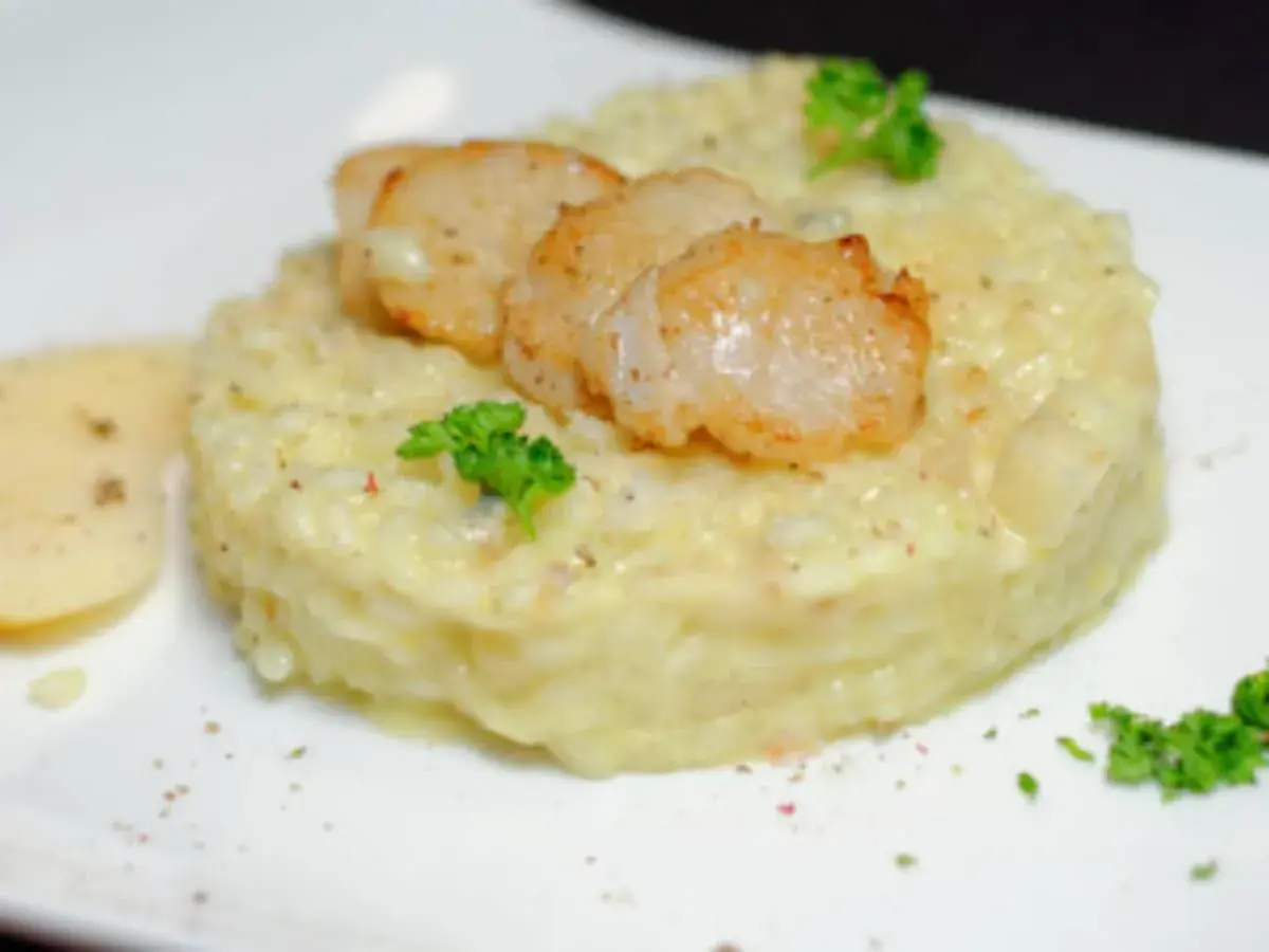 Un crémeux risotto poire gorgonzola, garni de Saint-Jacques poêlées et d'une touche de persil frais.