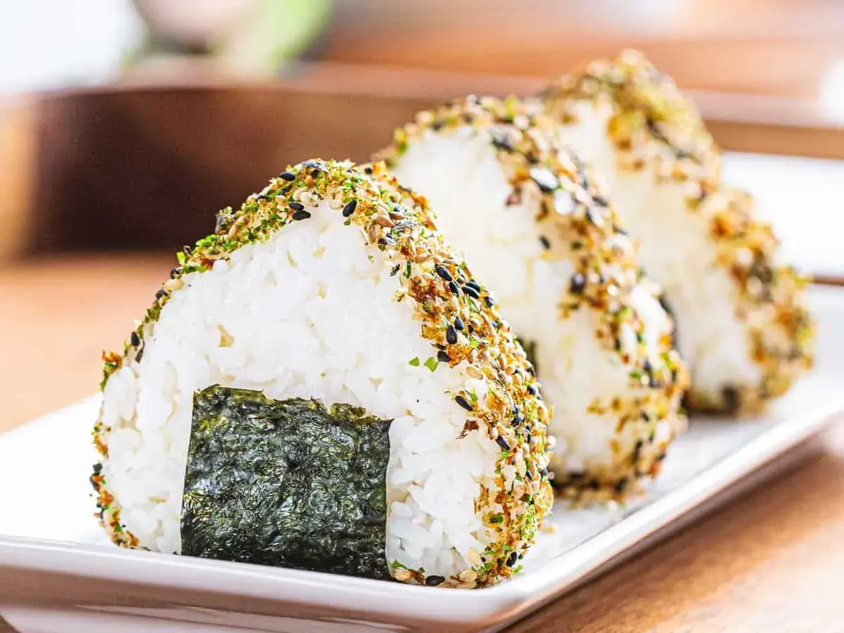Triangular onigiri rice balls, coated in furikake seasoning, showcase the best rice for onigiri. A piece of nori seaweed adorns the front.