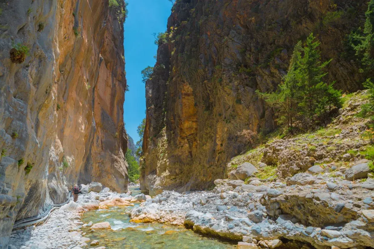 Wanderer in der Samaria Schlucht, umgeben von steilen Felswänden und einem klaren Flussbett.