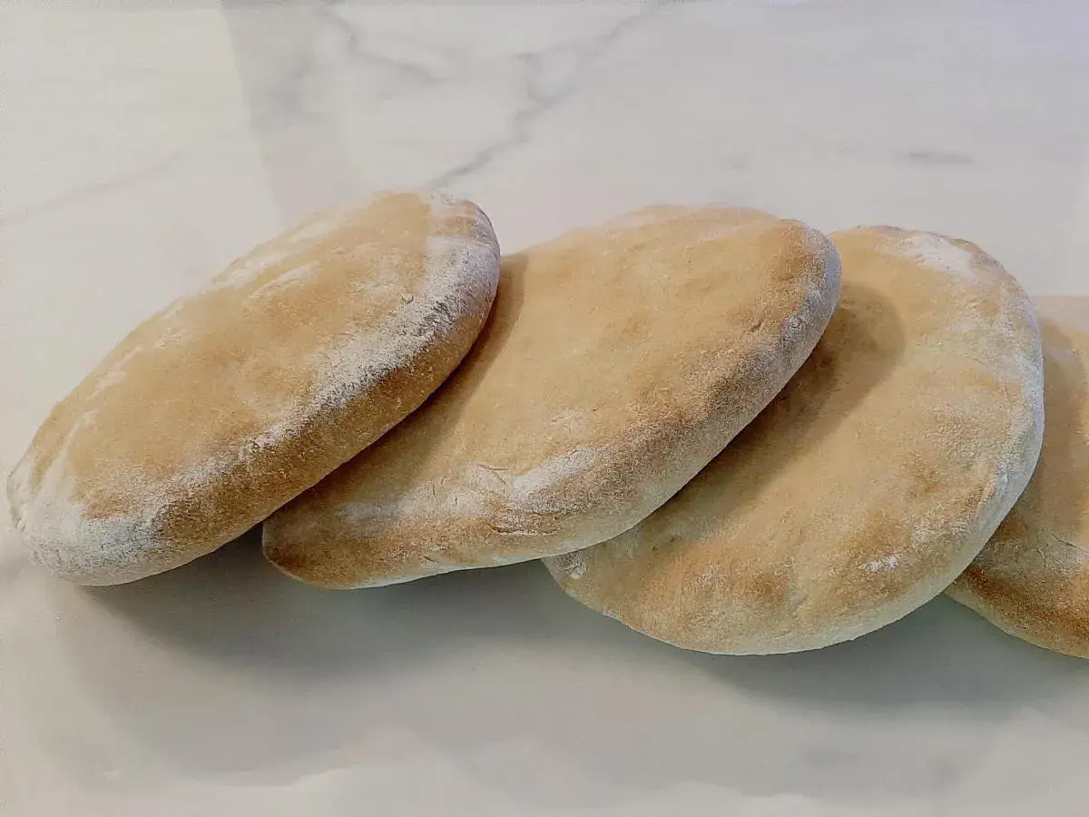 Quatre pains arabes dorés, légèrement saupoudrés de farine, prêts à être garnir.