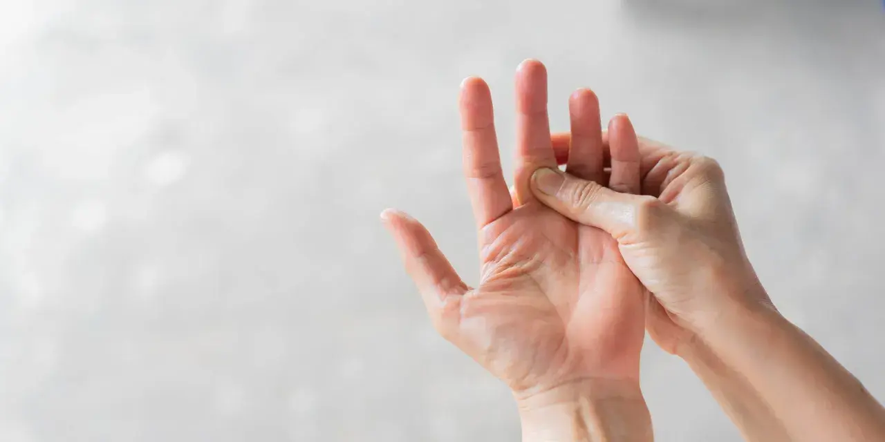 Hand massiert einen schmerzenden Finger, der auf eine Prellung hindeutet.