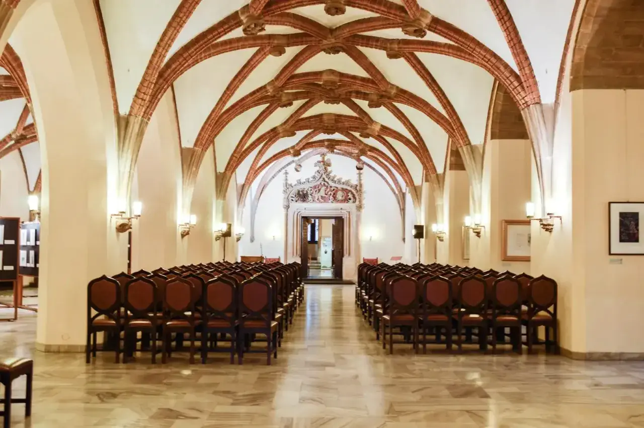 Wnętrze sali z rzędami krzeseł i ozdobnym sklepieniem.