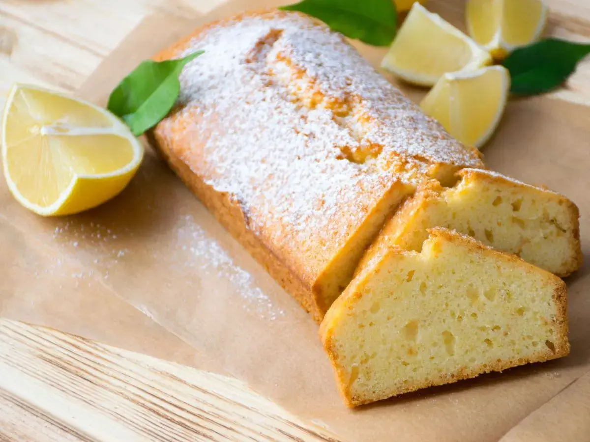 Saftiger veganer Zitronenkuchen, bestäubt mit Puderzucker, mit frischen Zitronenspalten und Blättern dekoriert.