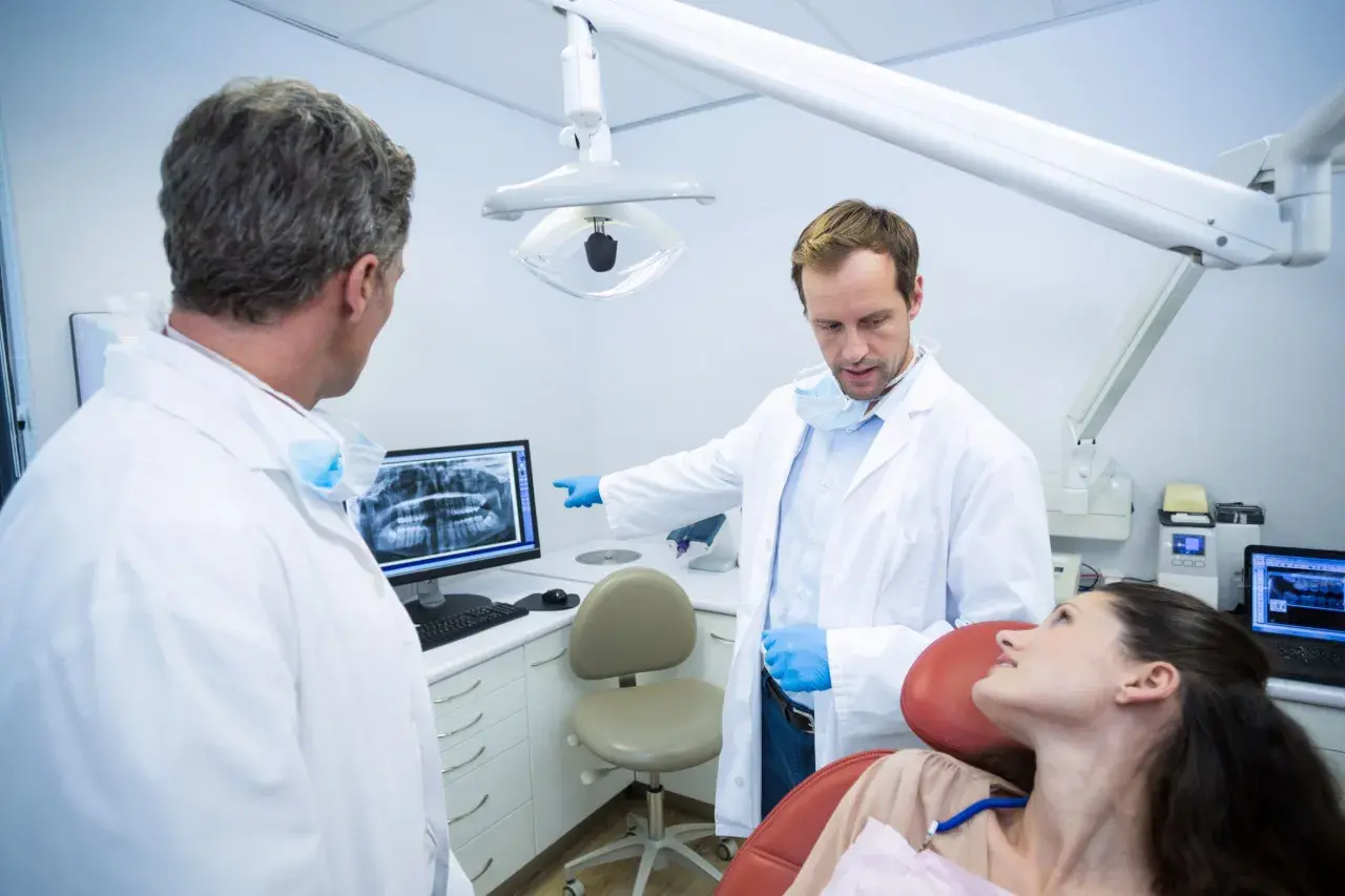 Dwóch dentystów omawia zdjęcie rentgenowskie z pacjentką, zastanawiając się, ile zarabia dentysta NFZ.