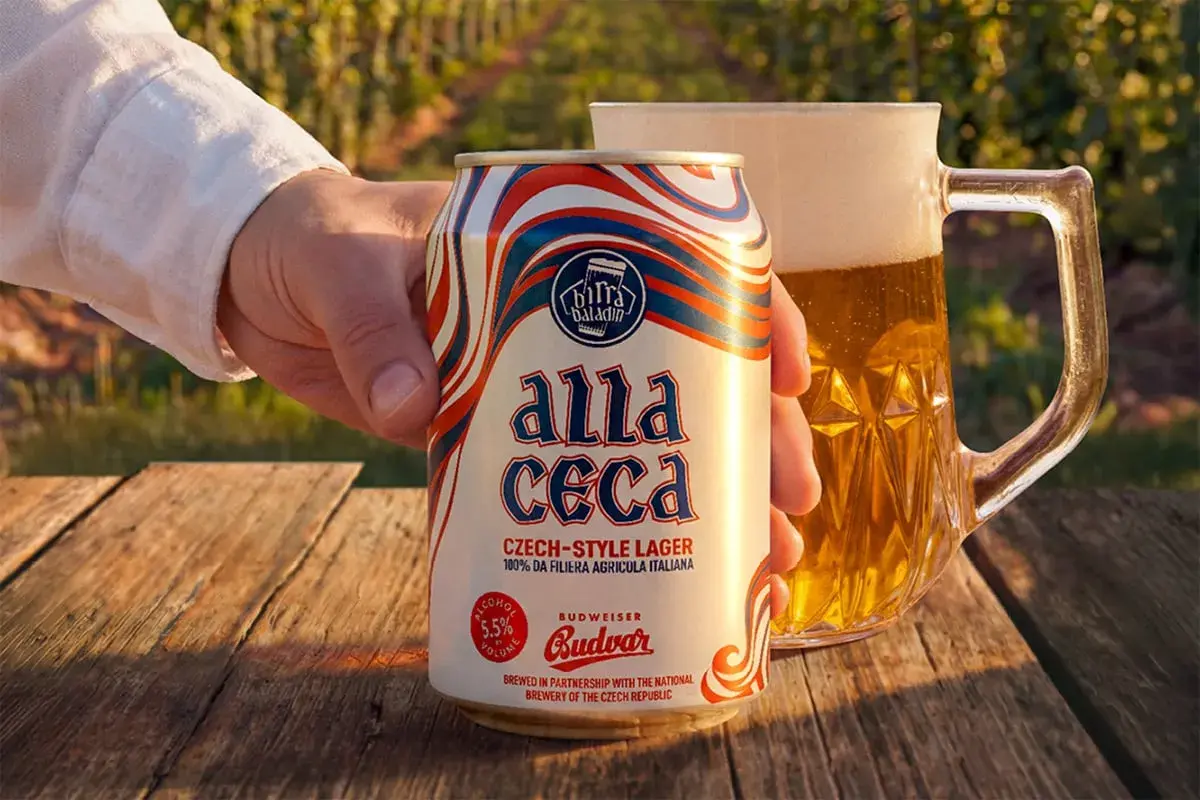 Mano che tiene una lattina di Budweiser ceca "Alla Ceca", con una birra in un boccale sullo sfondo.