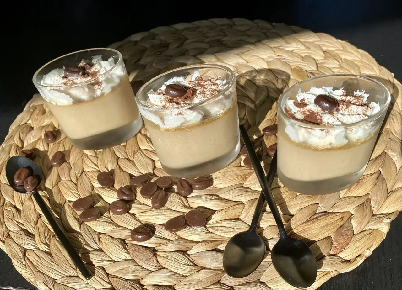 Trois verrines de crème au café facile, garnies de chantilly, cacao et grains de café. Des chocolats en forme de grains parsèment le napperon.