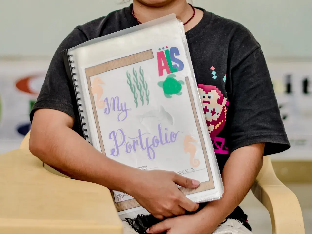 Ein Kind hält ein bunt gestaltetes Portfolio für den Kindergarten mit Seepferdchen und Schildkröten.
