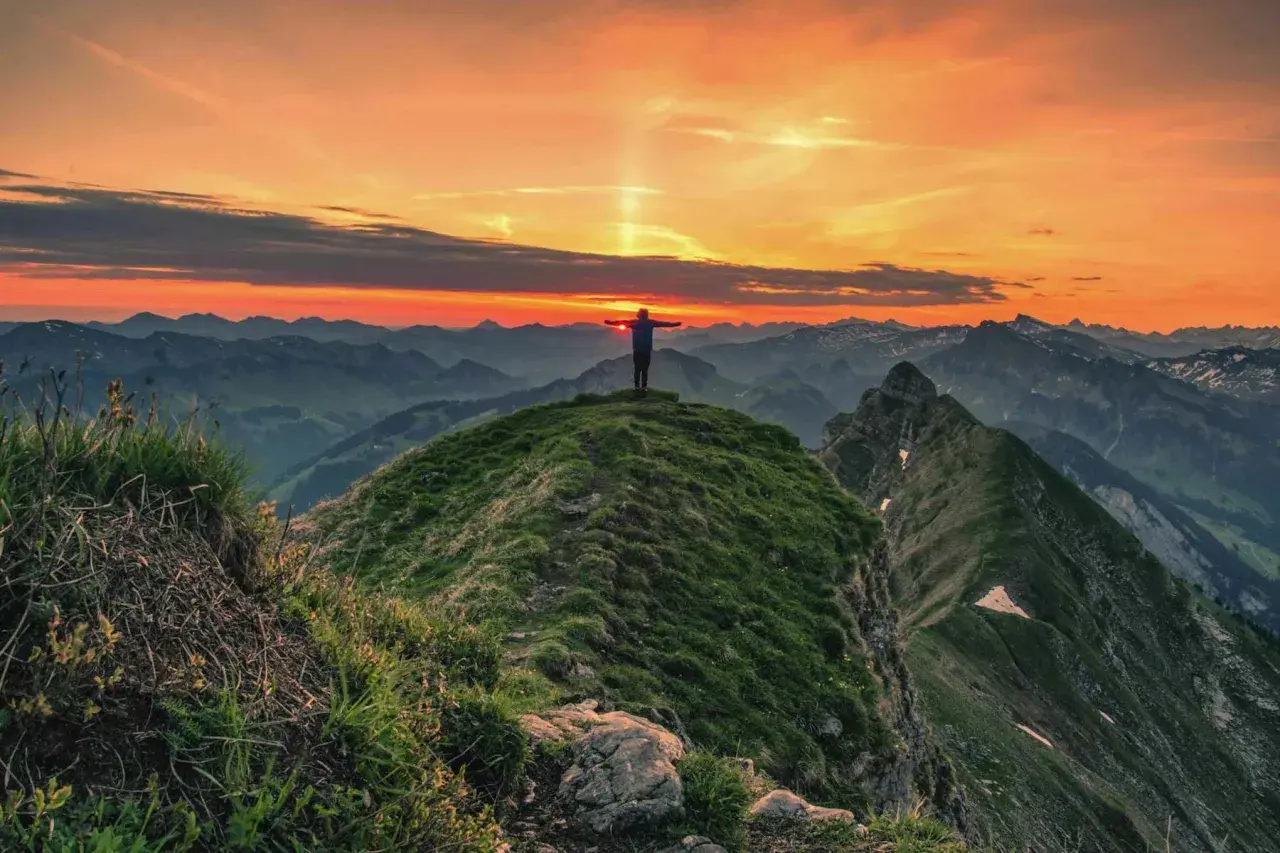 Sonnenuntergang auf der Kanisfluh Wanderung. Ein Wanderer steht mit ausgebreiteten Armen auf dem Gipfel und genießt den atemberaubenden Ausblick.