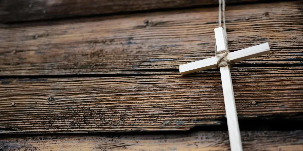 Ein hölzernes Kreuz, gebunden mit Seil, hängt vor einer rustikalen Holzvertäfelung. Ein Symbol für den Karfreitag, den Feiertag der Besinnung.