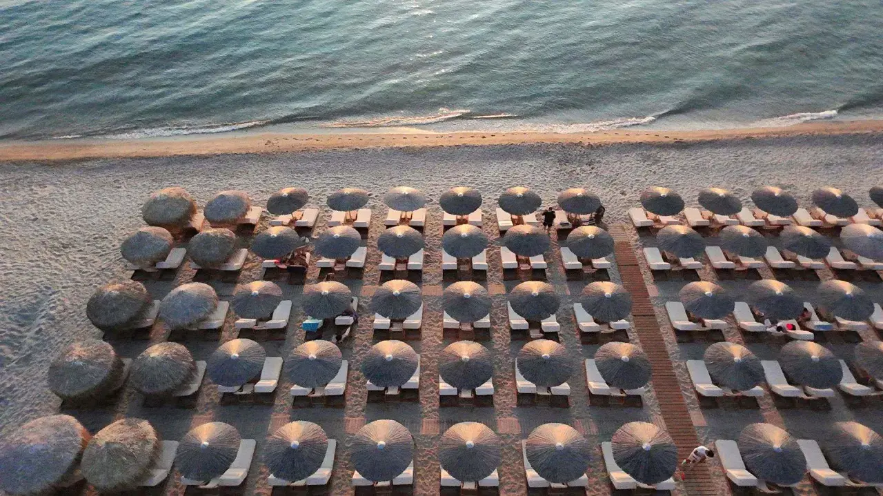 Rzędy leżaków pod słomianymi parasolami na plaży w Sithonii, z morzem w tle.