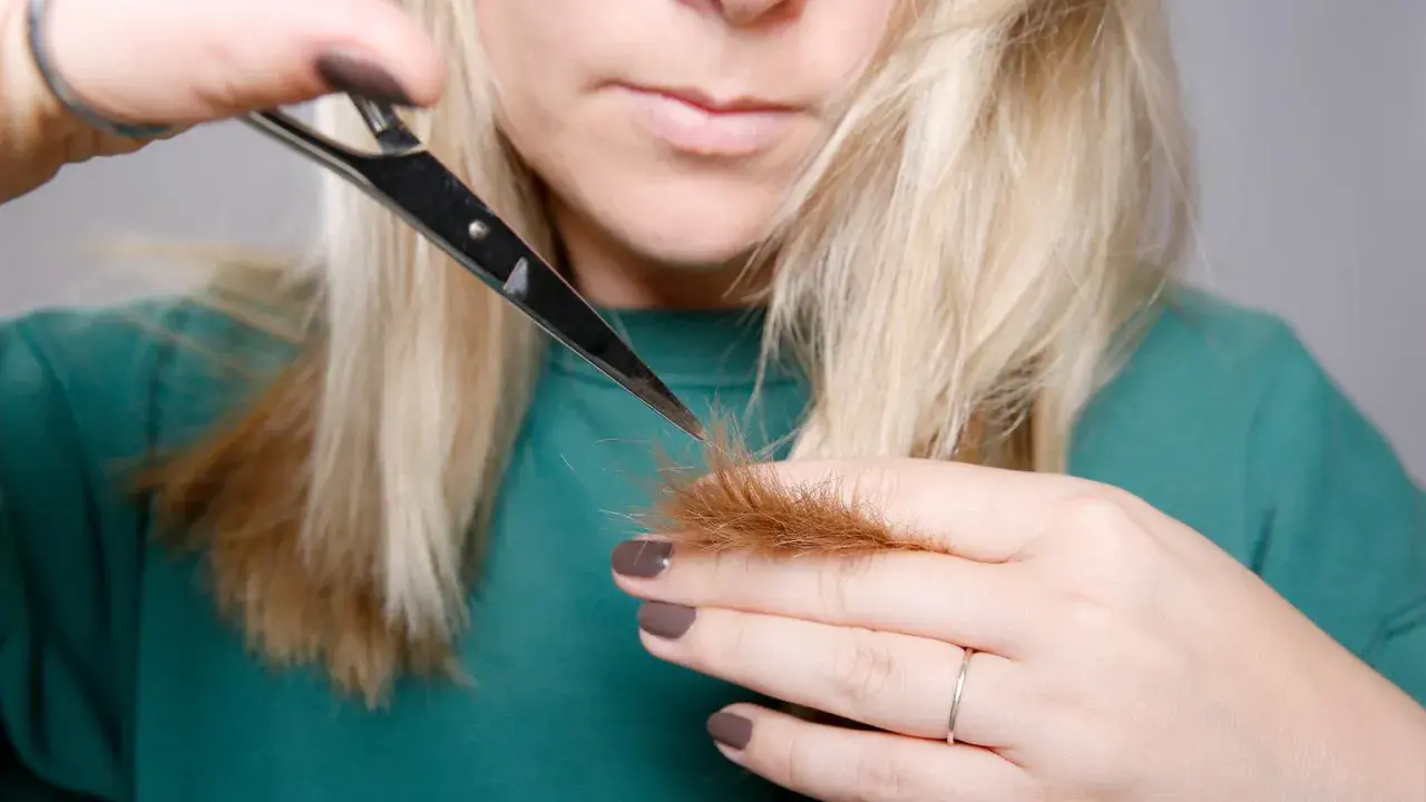 Kobieta z blond włosami podcina końcówki nożyczkami.