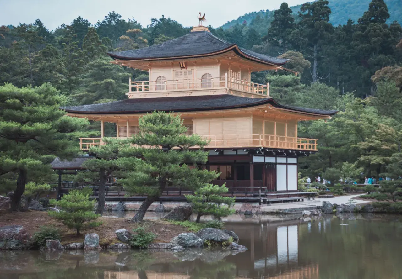 Złoty Pawilon Kinkaku-ji w Kioto, otoczony zielenią i odbijający się w stawie.