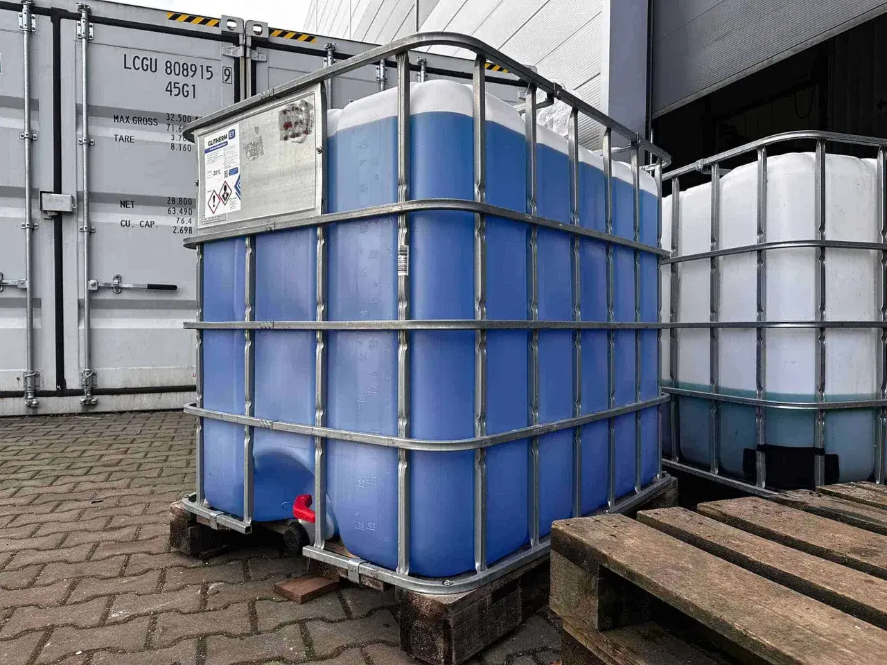 Duże kontenery IBC z niebieskim płynem, prawdopodobnie glikol etylenowy, czekają na transport. Właściwości glikolu etylenowego czynią go użytecznym w wielu zastosowaniach.