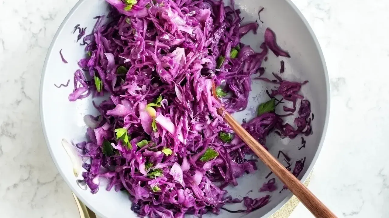 Insalata fresca di cavolo rosso, tagliato finemente e condito con erbe aromatiche, servita in una ciotola con un cucchiaio di legno.