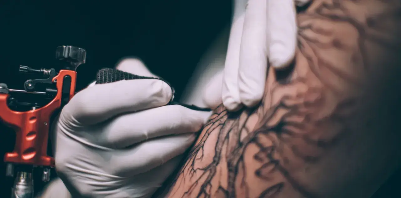 Dłoń w rękawiczce tworzy tatuaż metodą handpoke. To precyzyjne, ręczne tatuowanie, które daje unikalne efekty.