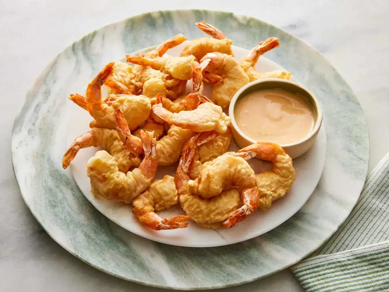 A plate piled high with golden-brown shrimp tempura, served with a small bowl of creamy dipping sauce.