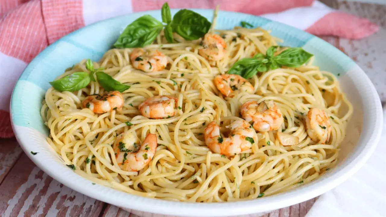 Un plato de espaguetis con gambas, adornado con hojas de albahaca fresca y perejil picado.