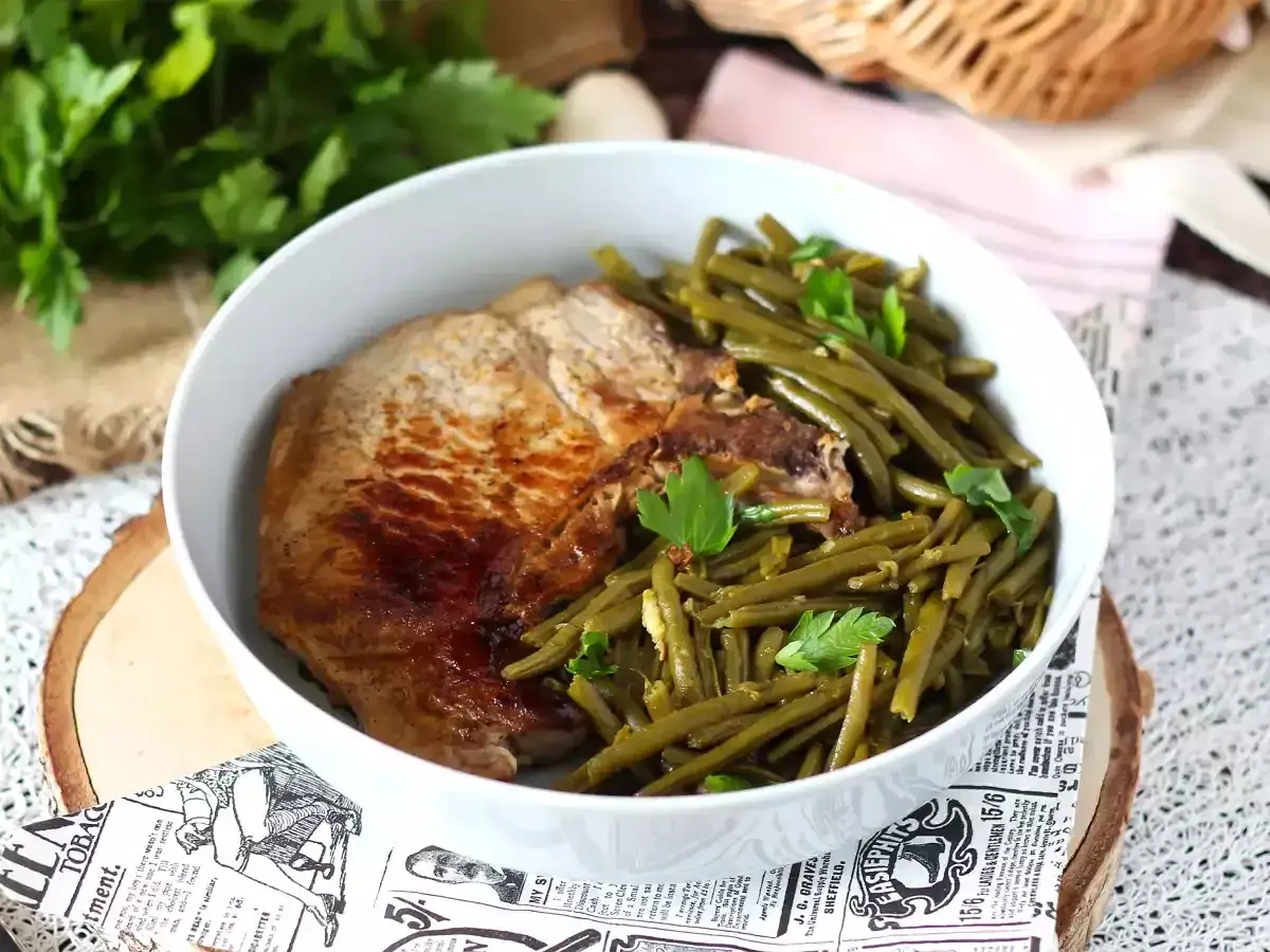 Une savoureuse côte de porc grillée accompagnée de haricots verts frais et persil, servie dans un bol blanc.