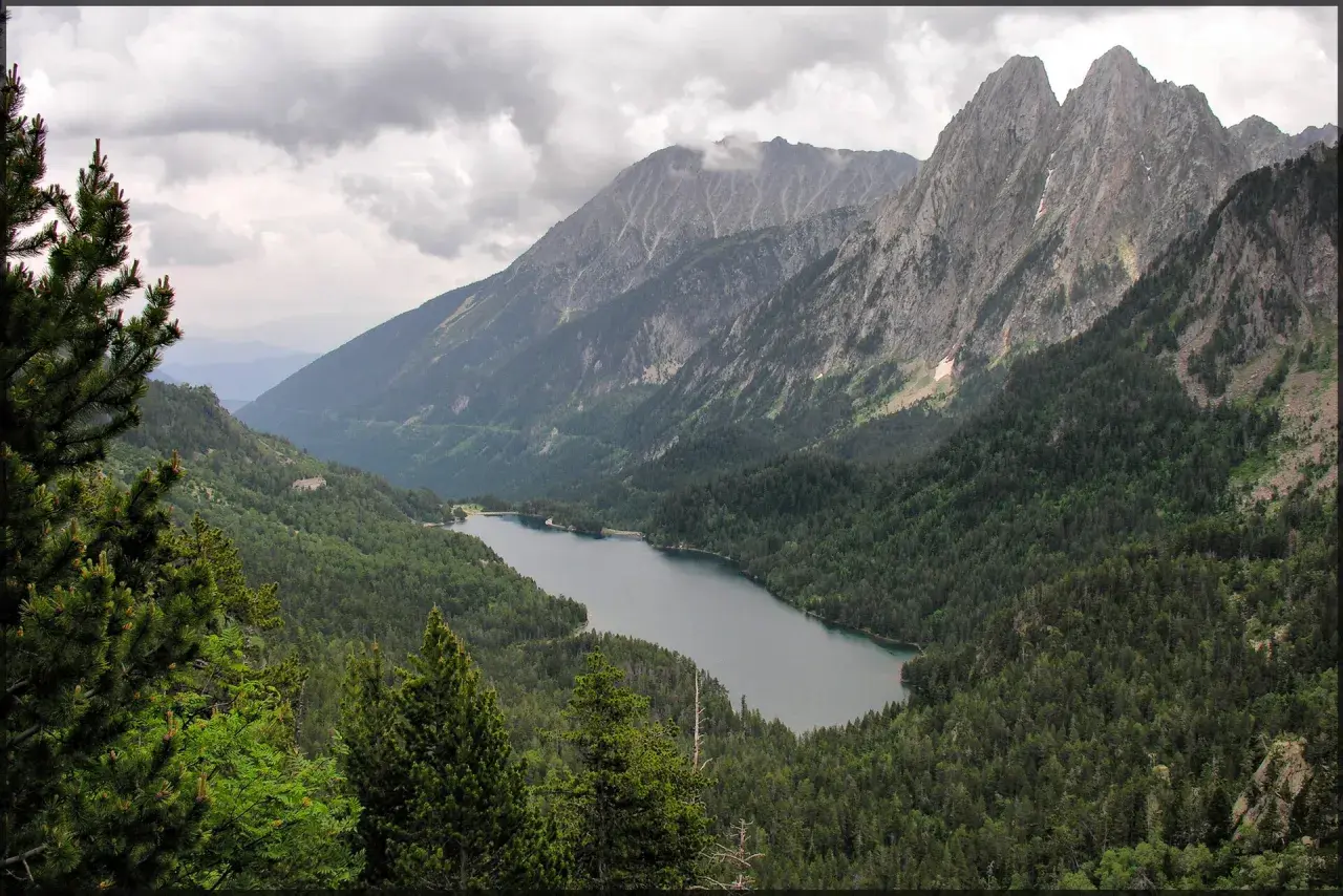 Paisaje montañoso con un lago sereno rodeado de bosques frondosos, ideal para explorar rutas desde Espot.