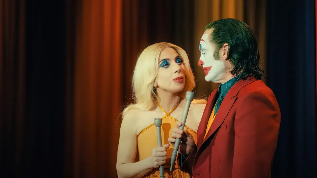 Joker e Harley Quinn, con microfoni in mano, si guardano intensamente. La trama del film si infittisce.