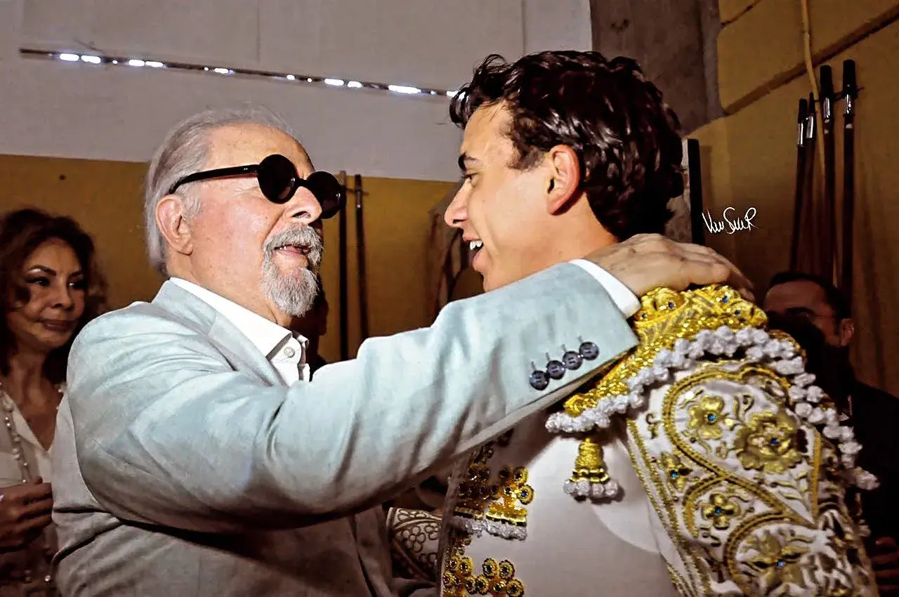 Un hombre mayor con gafas de sol abraza al torero Juan de Castilla, quien luce su traje de luces.