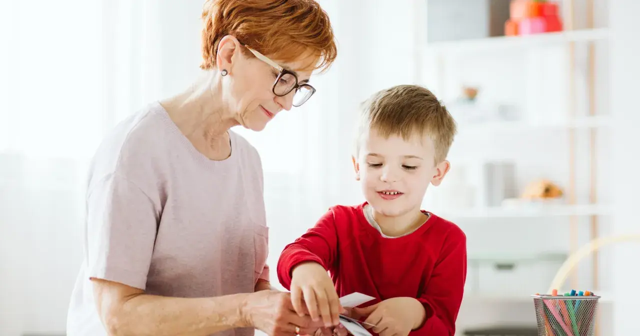 Babcia z wnukiem przeglądają karty, ucząc się rozpoznawać różne rzeczy. To świetny sposób na rozwijanie wiedzy i zapobieganie stereotypie u dzieci.